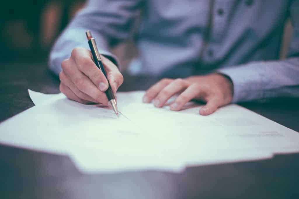 Professionally-dressed man writes on white paper.