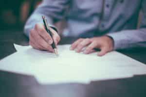 Professionally-dressed man writes on white paper.